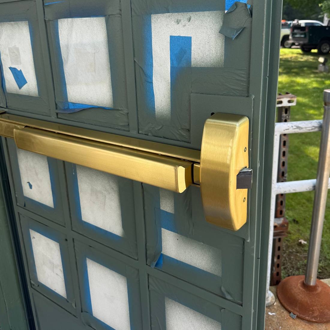 Brushed brass commercial panic exit bar installed on a green storefront door by Aura Locksmith in Brooklyn